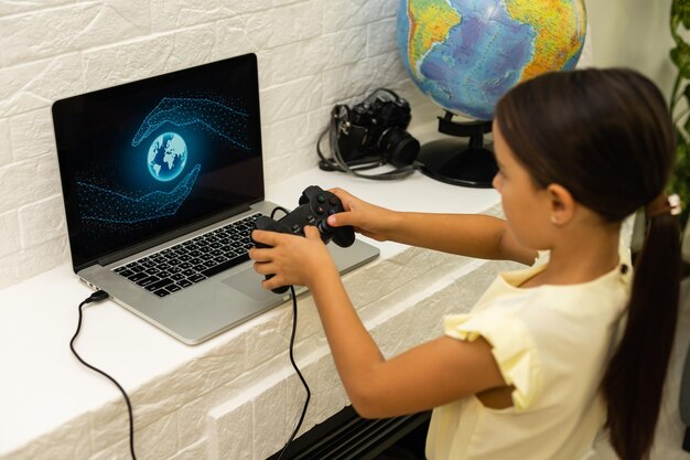 petite fille jouant à des jeux avec un ordinateur portable et un contrôleur de joystick