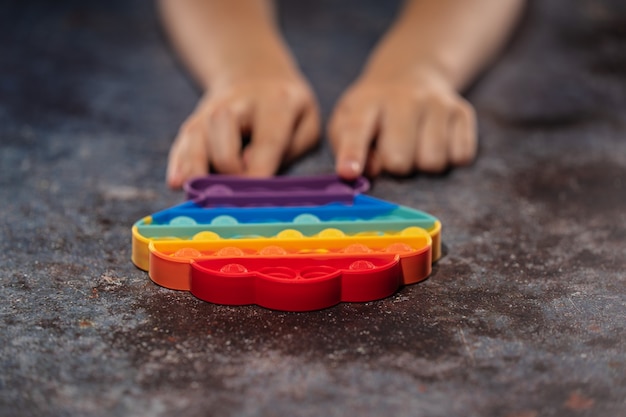 Photo petite fille jouant avec un jouet anti-stress en silicone pop it de couleur arc-en-ciel.