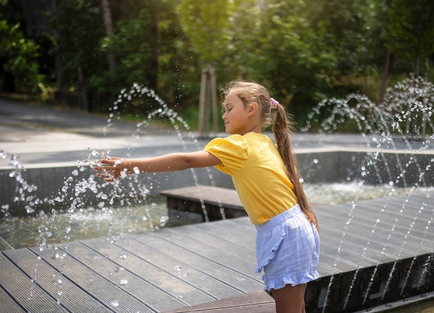 petite fille jouant avec de petites fontaines sur la place de la ville un chaud jour d'été