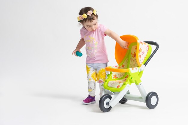 Une Petite Fille Jouant Avec Une Poussette Jouet Pour Poupées Sur Fond  Blanc Le Concept De L'enfance Des Jouets Pour Enfants