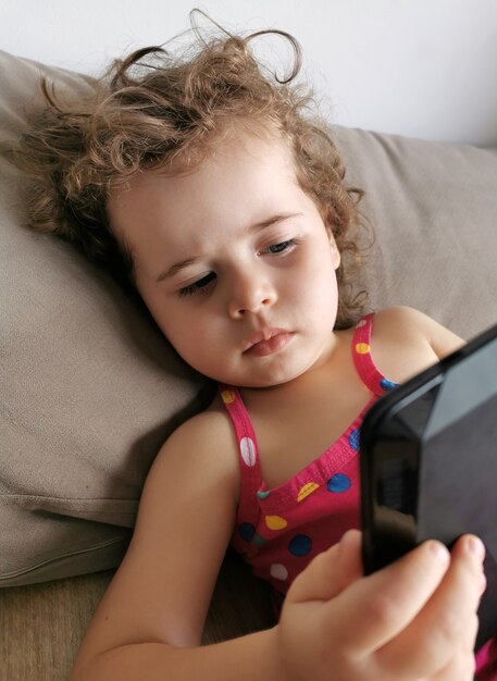 Petite fille jouant avec tablette sur canapé.