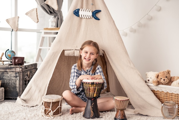 Petite Fille Jouant Sur Des Tambours De Djembé Africains Traditionnels Assis En Wigwam à La Maison