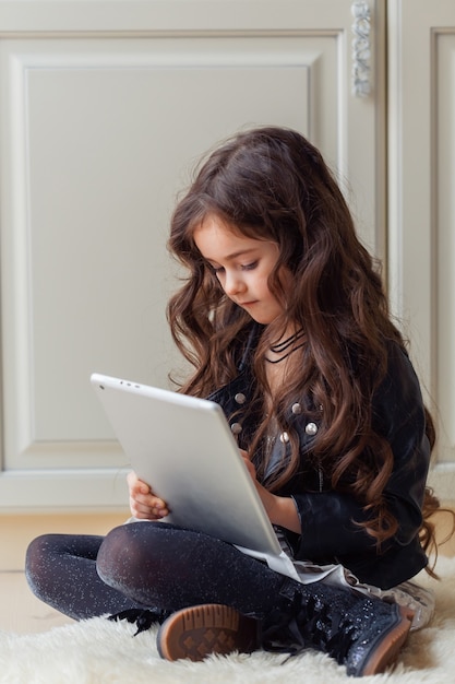 Petite fille joue au jeu à l'aide de la tablette alors qu'elle était assise sur le sol dans sa chambre