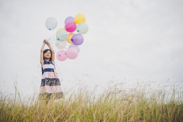 Une petite fille joue avec des ballons sur un champ de prairies.