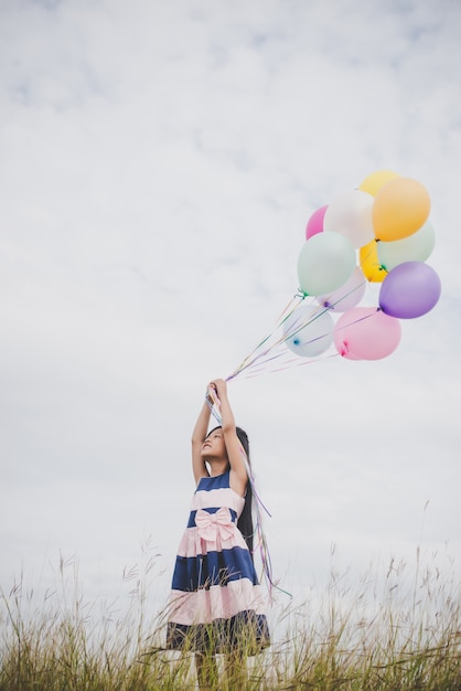 Une petite fille joue avec des ballons sur un champ de prairies.