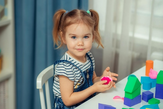 La petite fille joue avec des blocs de jouets colorés et construit une tour Jouets et jeux éducatifs et créatifs pour les jeunes enfants