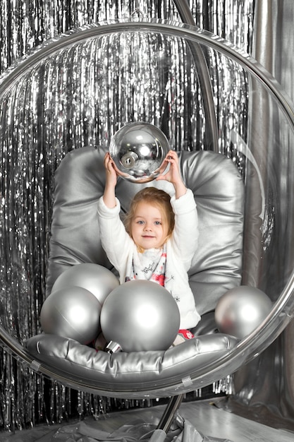 Petite fille joue sur une chaise un bol en verre avec des boules d'argent. Couverture de la reine des neiges.