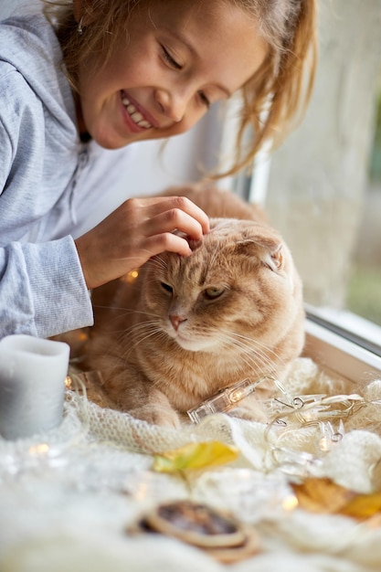 Petite fille joue avec un chat allongé sur le rebord de la fenêtre à la maison