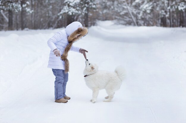 une petite fille joue avec un chien dans la forêt d'hiver