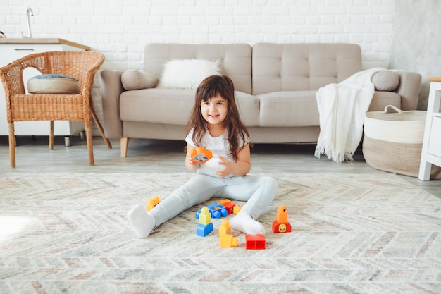 Une petite fille joue avec un constructeur de couleurs à la maison sur le sol