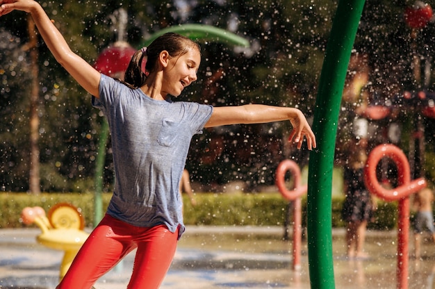 Petite fille joue avec des éclaboussures sur le terrain de jeu de l'eau dans le parc d'été. Loisirs des enfants dans le parc aquatique