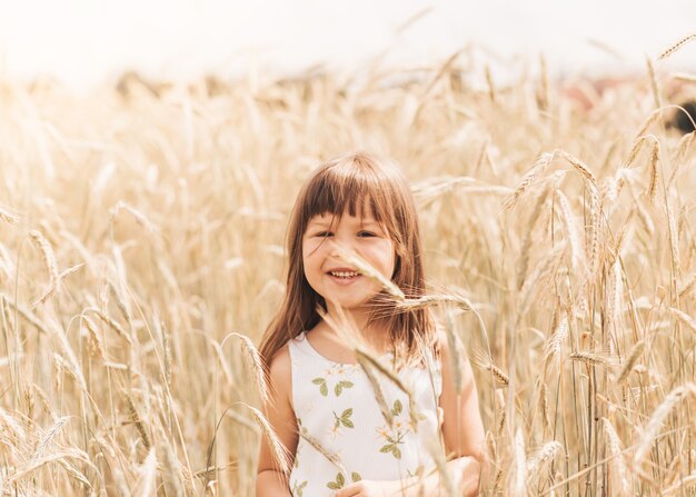 Une petite fille joue avec des épillets dans un champ de blé