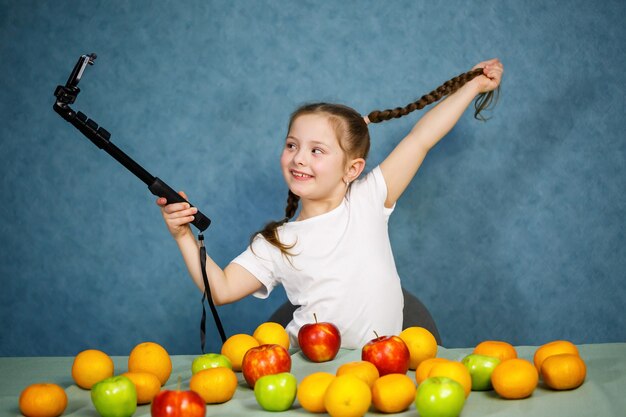 Petite fille joue avec des fruits et prend un selfie au téléphone. Vitamines et alimentation saine pour les enfants.