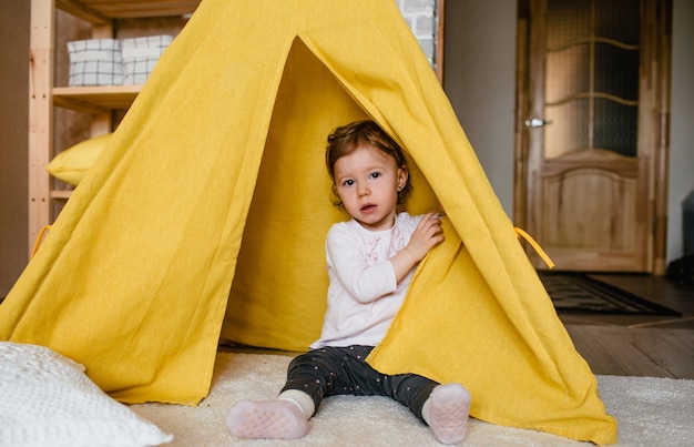 Une petite fille joue à l'intérieur d'un tipi jaune