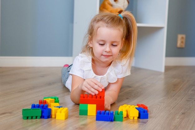 Une petite fille joue un kit de construction en plastique coloré à la maison sur le sol