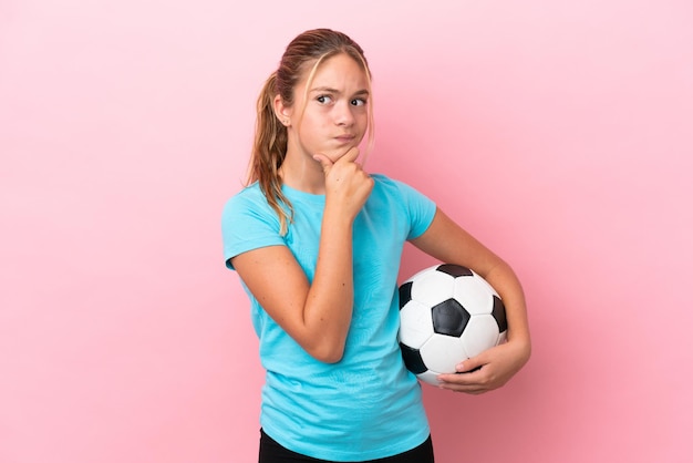 Petite fille de joueur de football isolée sur fond rose ayant des doutes et pensant
