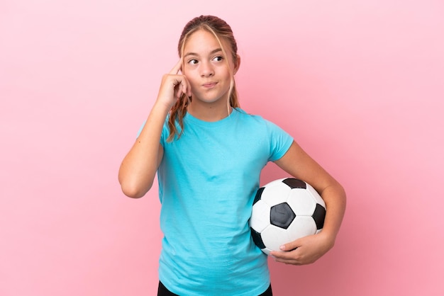 Petite fille de joueur de football isolée sur fond rose ayant des doutes et pensant