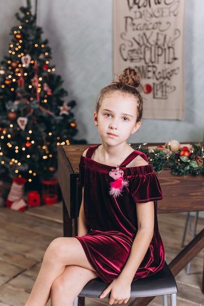 Petite fille joyeuse dans la décoration de Noël avec du thé à la maison confortable avec des lumières colorées du nouvel an