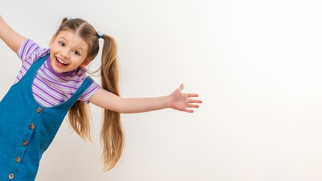 Une petite fille joyeuse dans une robe en jean sur une robe blanche.