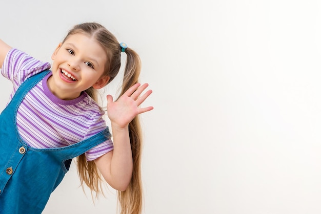 Une petite fille joyeuse dans une robe en jean sur une robe blanche.