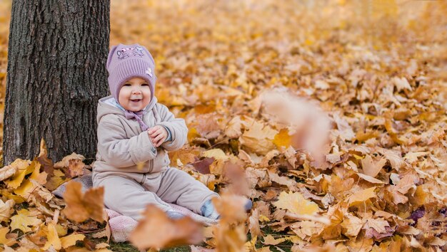 Petite fille joyeuse est assise sous un arbre au feuillage jaune d'automne. Copier l'espace