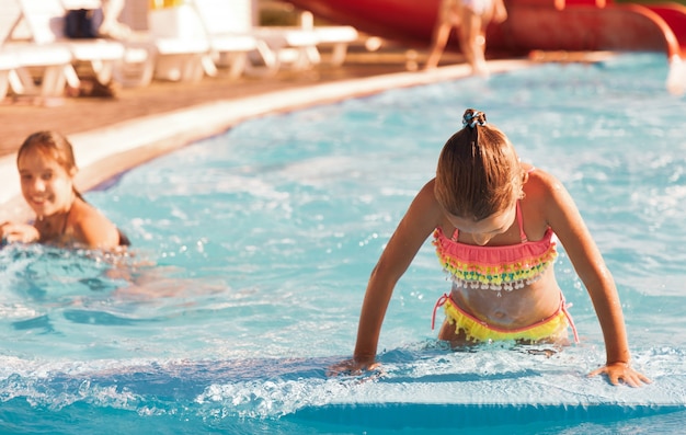 Petite fille joyeuse jouant dans la piscine avec de l'eau claire et claire et regardant la caméra en souriant