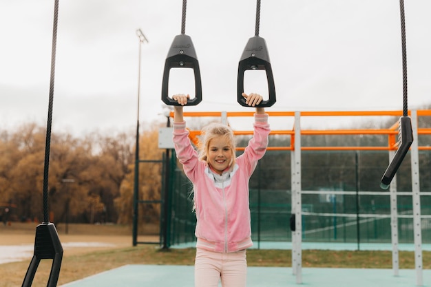 Petite fille joyeuse joue sur le terrain de jeu. L'enfant est engagé sur des anneaux de gymnastique dans la rue. L'enfant fait du sport sur des simulateurs.