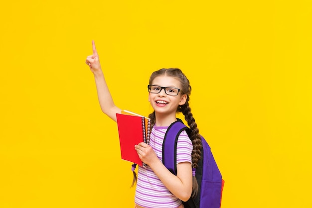 Une petite fille joyeuse tient des cahiers dans sa main et pointe vers le côté votre publicité