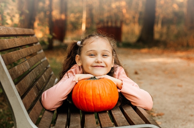 Une petite fille joyeuse tient une citrouille orange dans le parc à l'automne. Accessoires d'Halloween