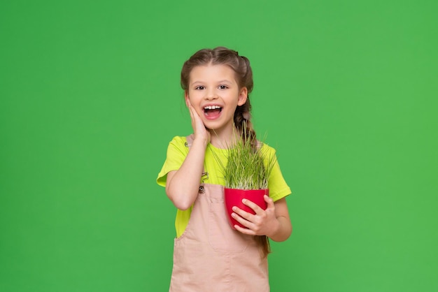 Une petite fille joyeuse tient un pot en céramique avec une plante à la main. Un enfant sur un fond vert isolé.