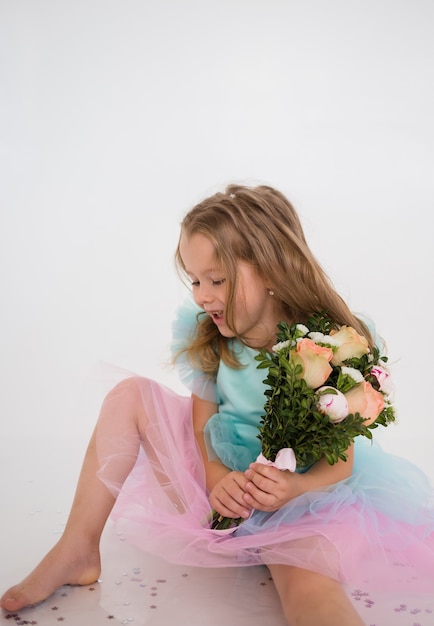 Une petite fille joyeuse vêtue d'une robe de fête tient un bouquet de fleurs fraîches sur fond blanc