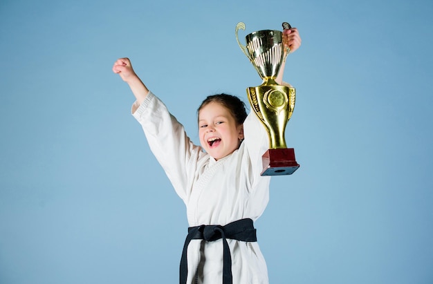 Petite fille en kimono blanc avec ceinture. Enfant de combattant de karaté. Concept de sport de karaté. Compétences d'autodéfense. Le karaté donne un sentiment de confiance. Petit enfant fort et confiant. Victoire et victoire.