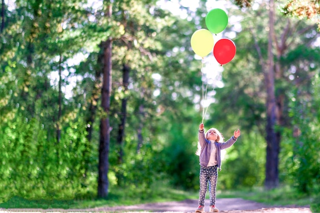 La petite fille laisse les ballons dans le ciel Dans la forêt d'été