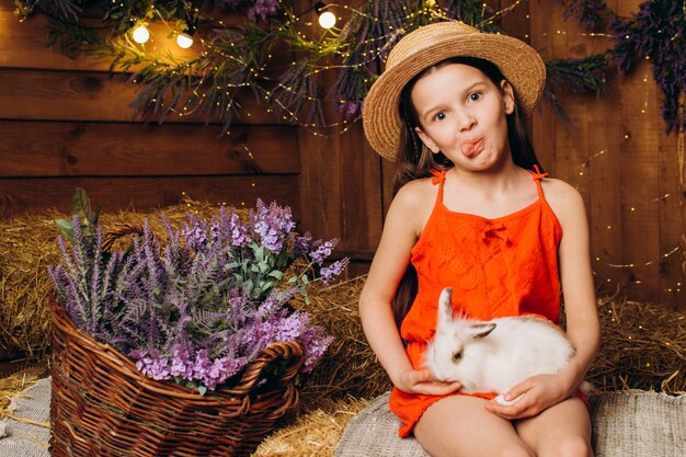 Petite fille avec un lapin dans une ferme sur fond de foin et de lavande