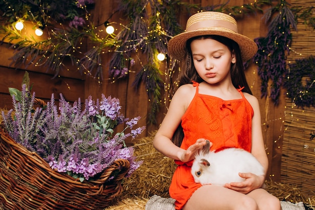 Petite fille avec un lapin dans une ferme sur fond de foin et de lavande