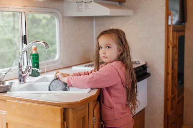 Petite fille lavant la vaisselle dans la cuisine d'une caravane