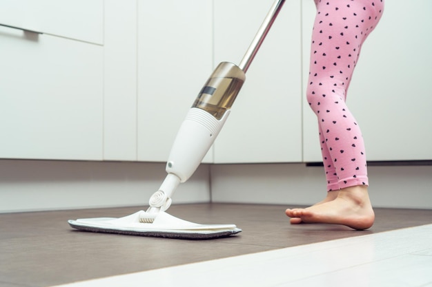 Petite fille laver le sol par une vadrouille moderne avec une brosse amovible et un réservoir d'eau près de la cuisine en gros plan photo recadrée