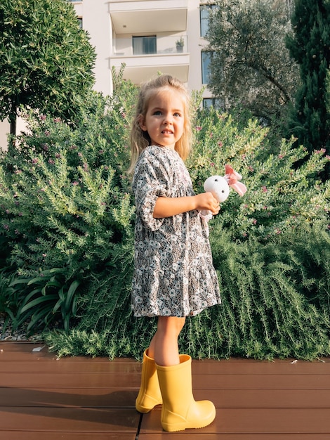 Petite fille avec un lièvre jouet se tient près d'un buisson de genévrier en fleurs