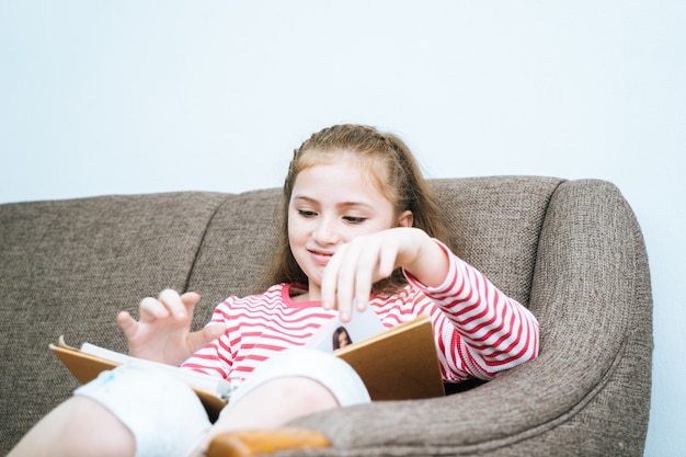 Petite fille lit un livre sur le canapé