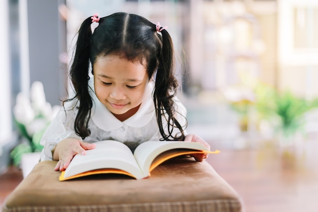 Photo petite fille lit un livre dans sa chambre. concept d'enfants de l'éducation.