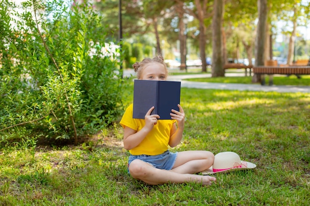 Une petite fille lit un livre sur l'herbe dans le parc en été