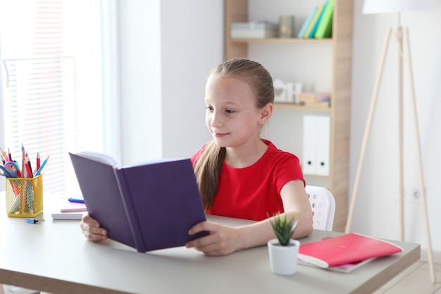 La petite fille lit un livre à la maison