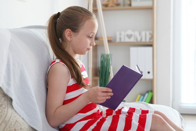 La petite fille lit un livre à la maison