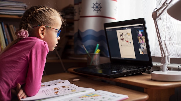 Petite fille à lunettes étudiant en ligne et en utilisant son ordinateur portable à la maison