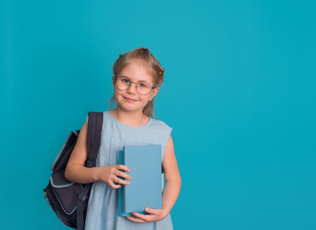 Petite fille à lunettes avec livres et sac à dos sur fond bleu