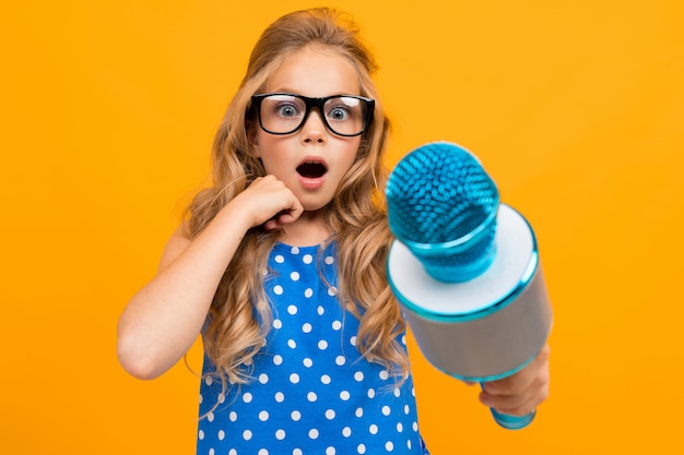 Une petite fille à lunettes avec un microphone est interviewée, la photo est isolée sur un mur jaune