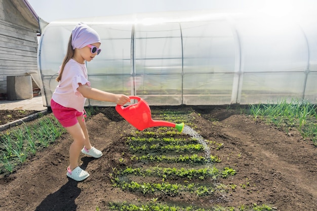 Petite fille à lunettes de soleil arrosant des plantes dans le jardin