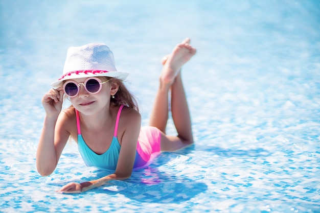 Petite fille à lunettes de soleil et chapeau avec licorne dans la piscine extérieure du complexe de luxe
