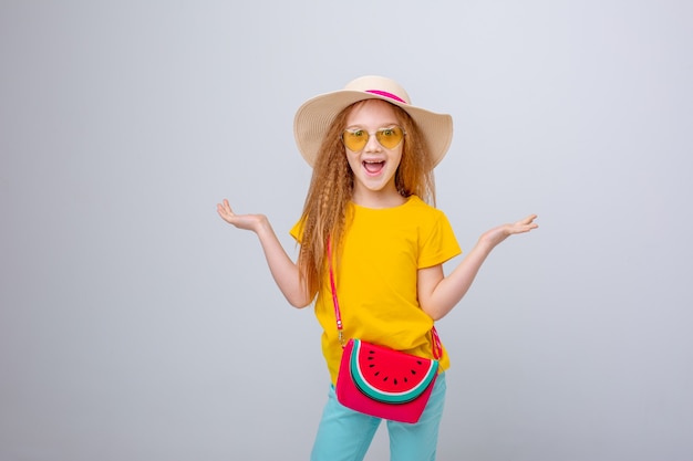 Une petite fille à lunettes de soleil et un chapeau de voyageur sur fond blanc