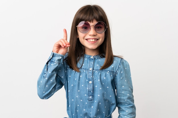 Petite fille avec des lunettes de soleil isolé sur fond blanc pointant vers le haut une excellente idée